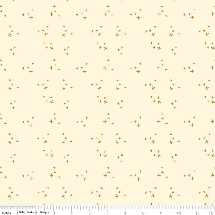 Scatter Cream fabric with small golden-orange crosses arranged in loose clusters on a pale cream background with ruler for scale.