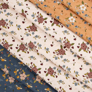 Folded fabrics with delicate floral prints arranged diagonally. The fabrics feature floral motifs in dusty pink, blue, yellow, and white on cream, peach, and navy backgrounds.