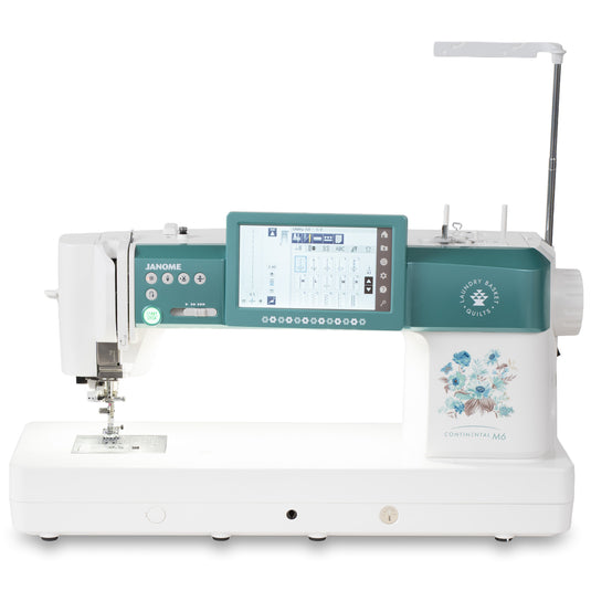 A Janome Continental M6 sewing machine in white and teal, featuring a digital touchscreen display, floral graphic on the front, and an extended arm, shown against a solid white background.