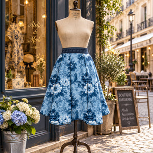 A blue floral skirt displayed on a beige mannequin outdoors in front of a boutique storefront. The skirt has a dark blue waistband and features a medium and light blue floral pattern.