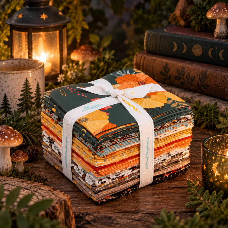 A stack of patterned fabric squares tied with a white ribbon, displayed on a rustic wooden surface with candles, books, mushrooms, and greenery in a cozy styled setting.
