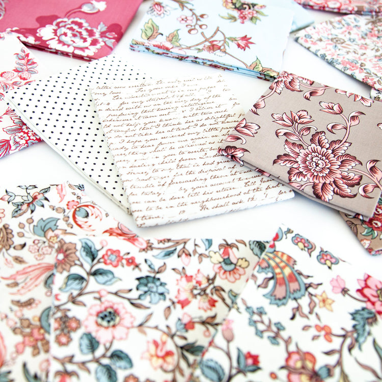 A styled flat-lay of multiple fabric swatches with various patterns, including floral prints, polka dots, and cursive script, arranged on a white surface.