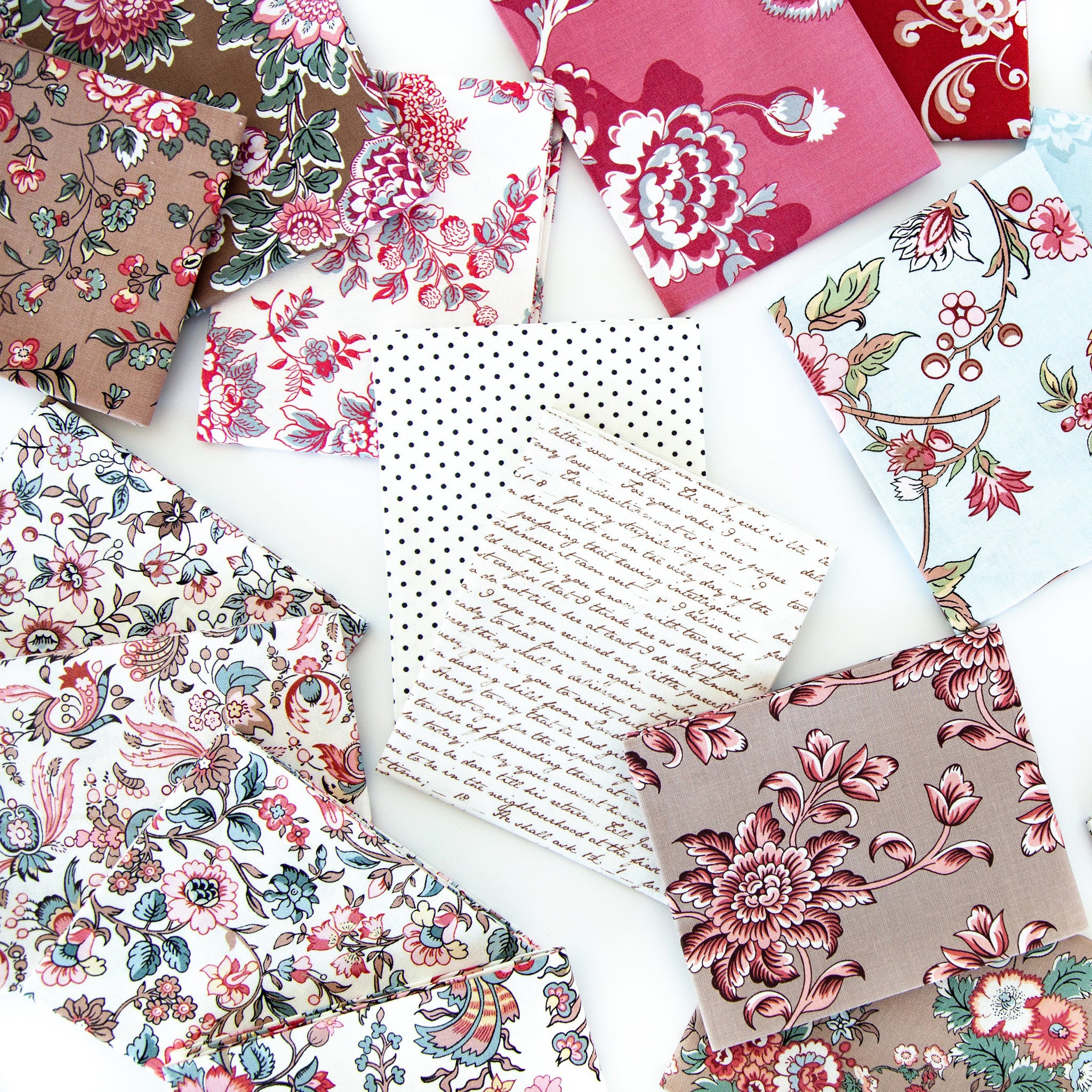 A styled flat-lay arrangement of multiple fabric napkins or small fabric squares with different prints, including floral, paisley, polka dots, and cursive script, spread out on a white background.