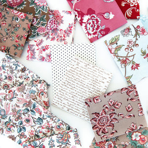 A styled flat-lay arrangement of multiple fabric napkins or small fabric squares with different prints, including floral, paisley, polka dots, and cursive script, spread out on a white background.