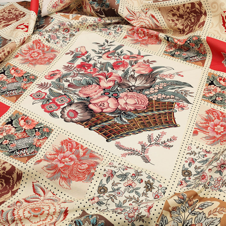 A close-up of a fabric featuring a patchwork design with floral motifs, peonies, and a central basket bouquet print in muted red, pink, beige, brown, and gray tones.