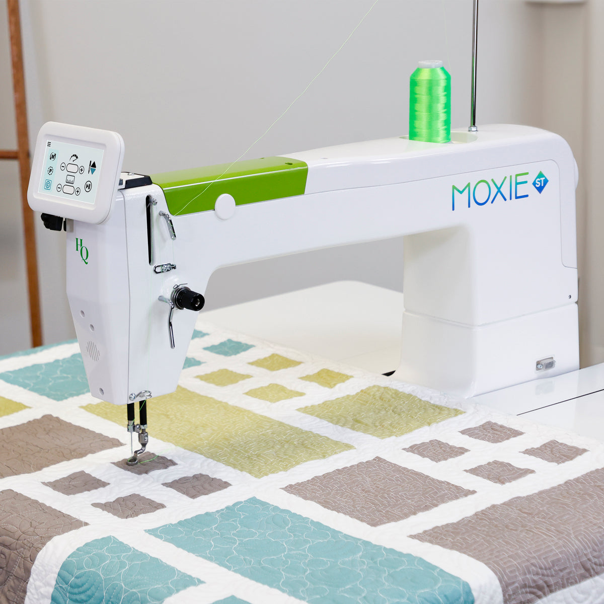 Moxie ST machine with green accents, shown in a bright indoor setting with a colorful quilt underneath and a spool of green thread on top.
