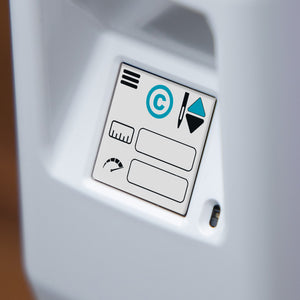 Close-up of a white electronic device showing a small printed control panel with icons, including a circular C symbol, on a white surface.