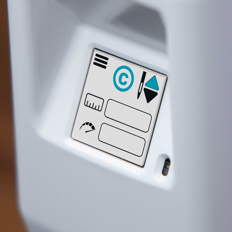 Close-up of a white electronic device showing a small printed control panel with icons, including a circular C symbol, on a white surface.