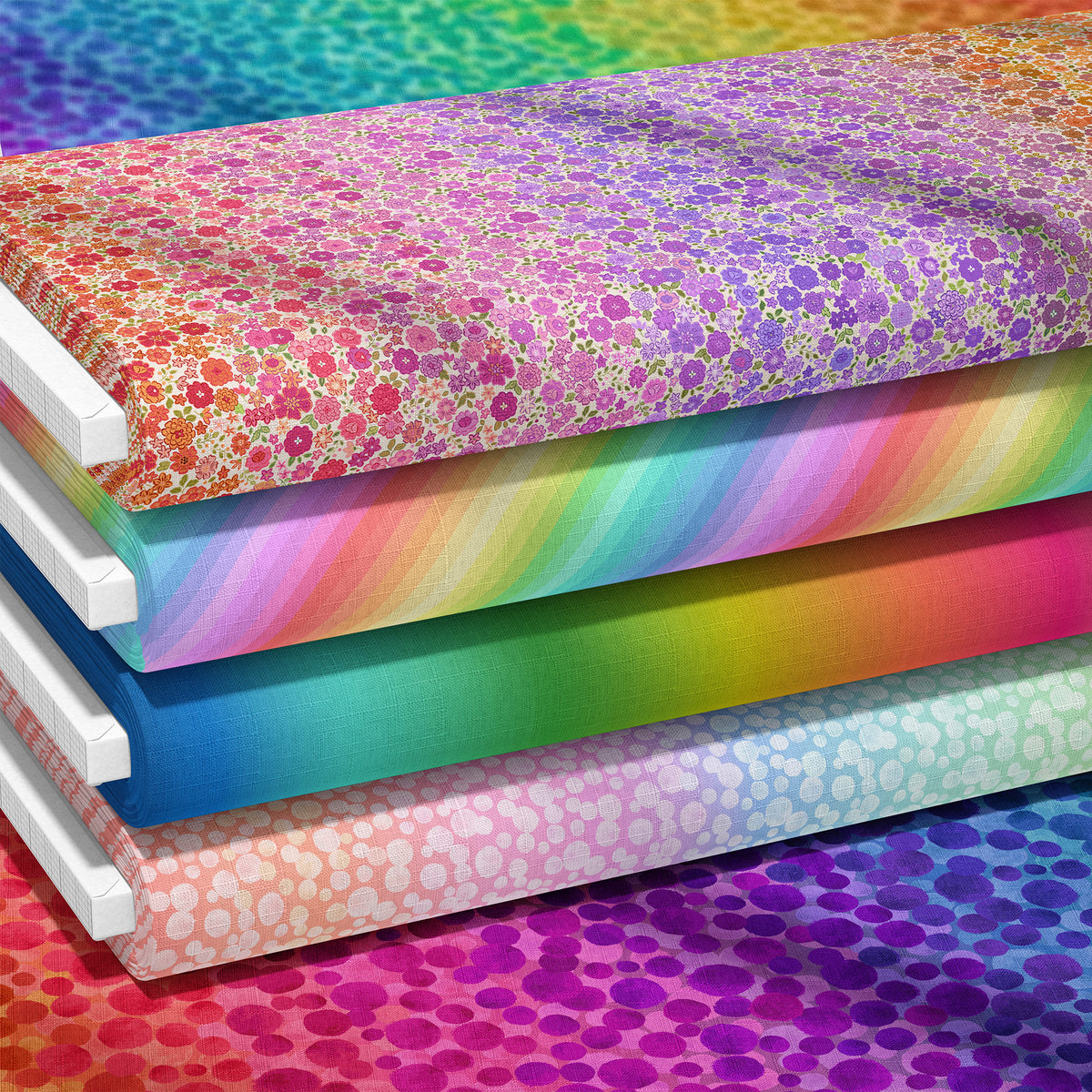 Stacked bolts of colorful patterned fabric with rainbow gradients and floral dot prints, shown on a white background with additional matching material visible behind them.