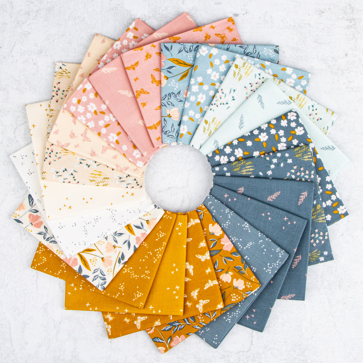 A circular arrangement of patterned fabric swatches in soft pastel and earthy tones, including pink, blue, mustard yellow, cream, and gray floral and leaf prints, displayed on a light textured background.