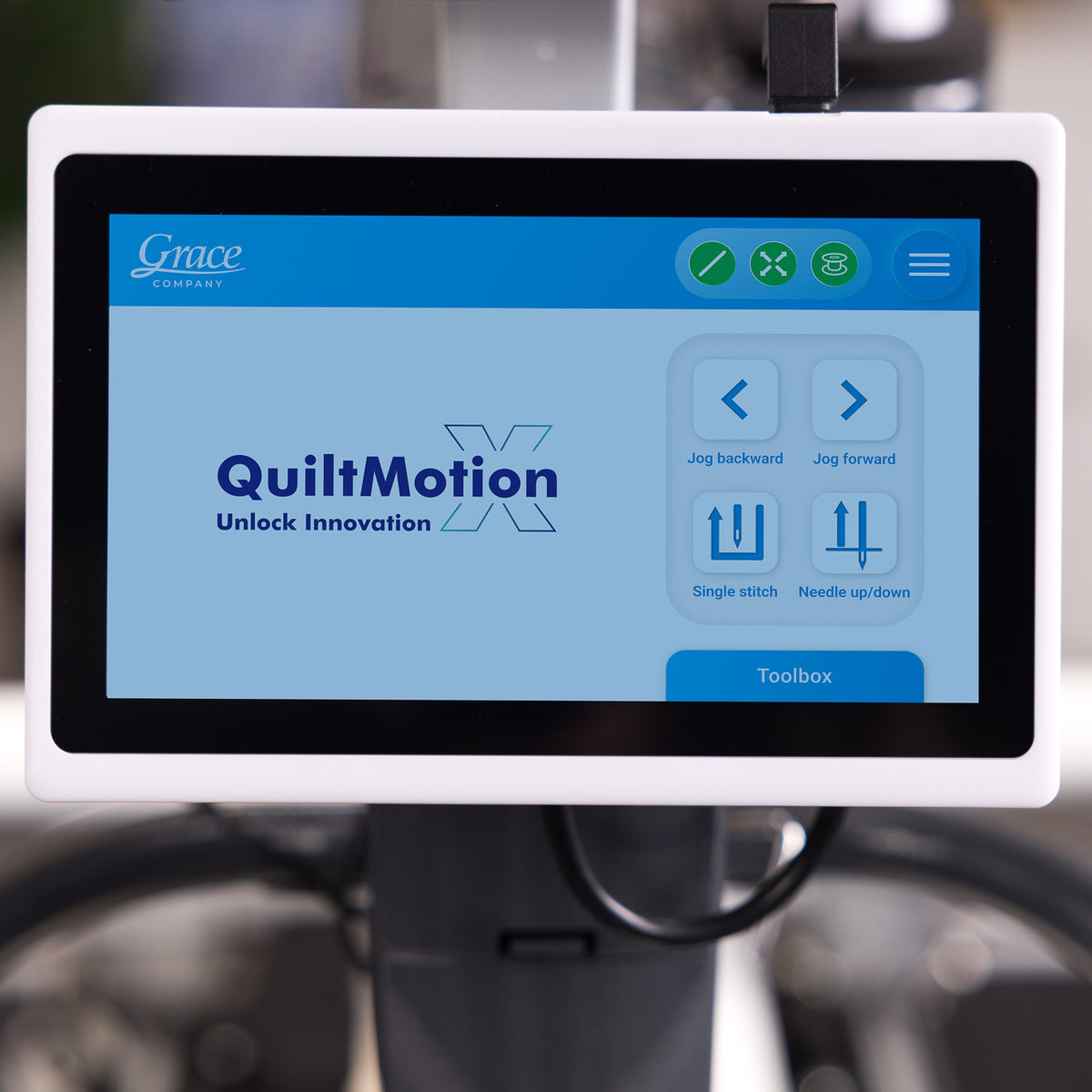 A Grace QuiltMotion X digital control screen mounted on a sewing machine, showing the user interface with options for jog directions and stitch settings.