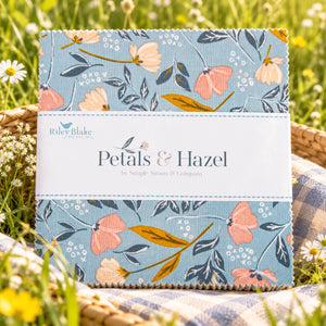 Close-up of Petals & Hazel 5-inch Stacker with blue floral fabric and a white Riley Blake Designs label laid outside in the grass.