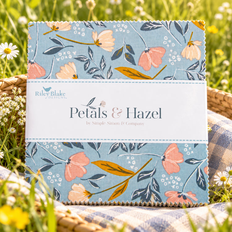 Close-up of Petals & Hazel 5-inch Stacker with blue floral fabric and a white Riley Blake Designs label laid outside in the grass.