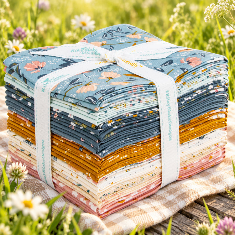 A floral fabric bundle placed on a wooden surface outdoors with grass and small white flowers in background.
