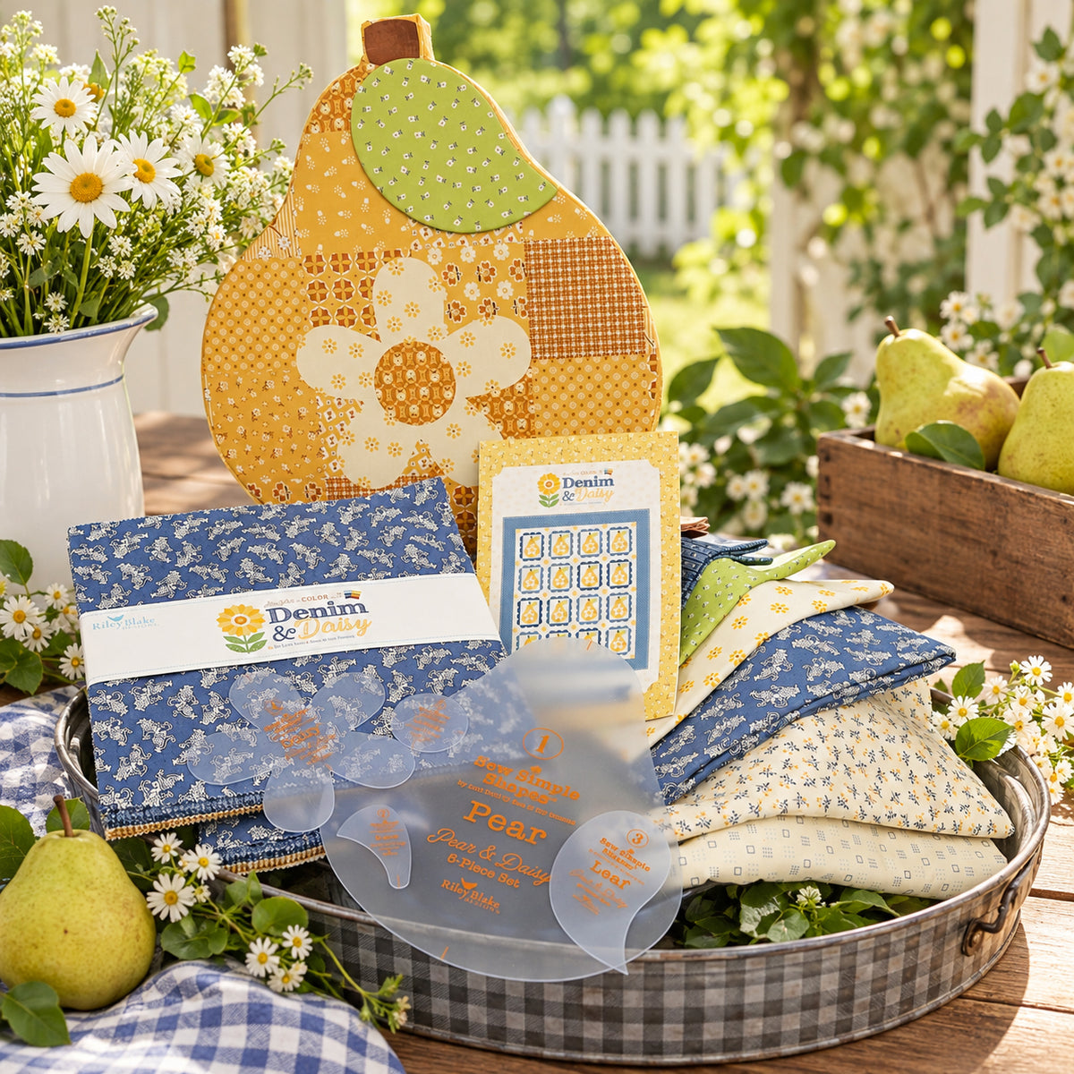 A quilt kit featuring a pear keepsake box, fabrics, pattern and template set. It is displayed outside among flowers and pears on a table.