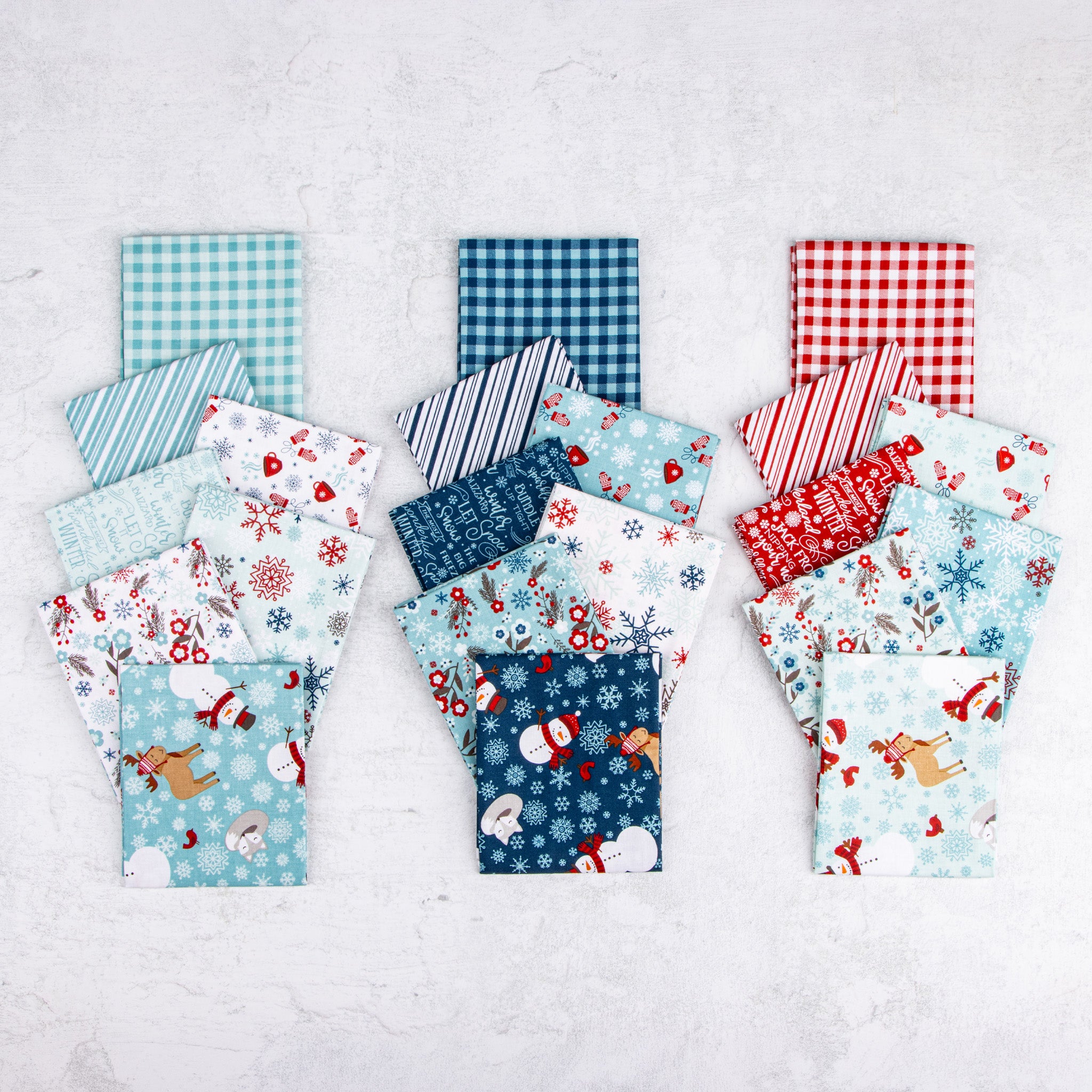 A Perfect Winter fabric assortment featuring coordinating red, navy, and icy blue prints with snowmen, reindeer, snowflakes, winter florals, gingham checks, and stripes.