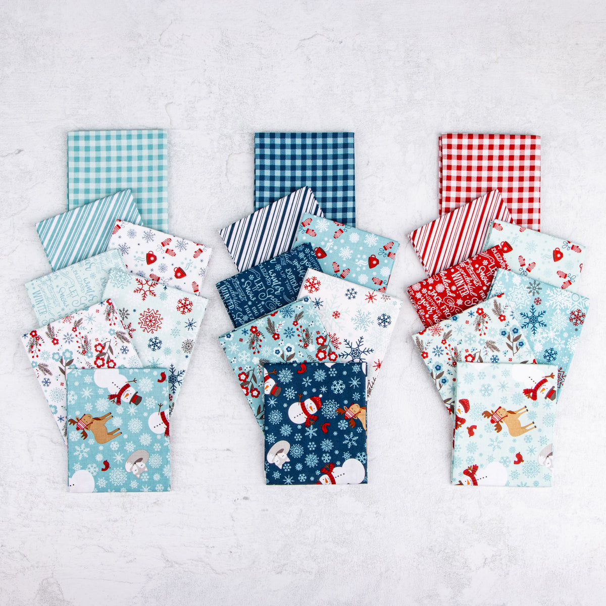 A Perfect Winter fabric assortment featuring coordinating red, navy, and icy blue prints with snowmen, reindeer, snowflakes, winter florals, gingham checks, and stripes.