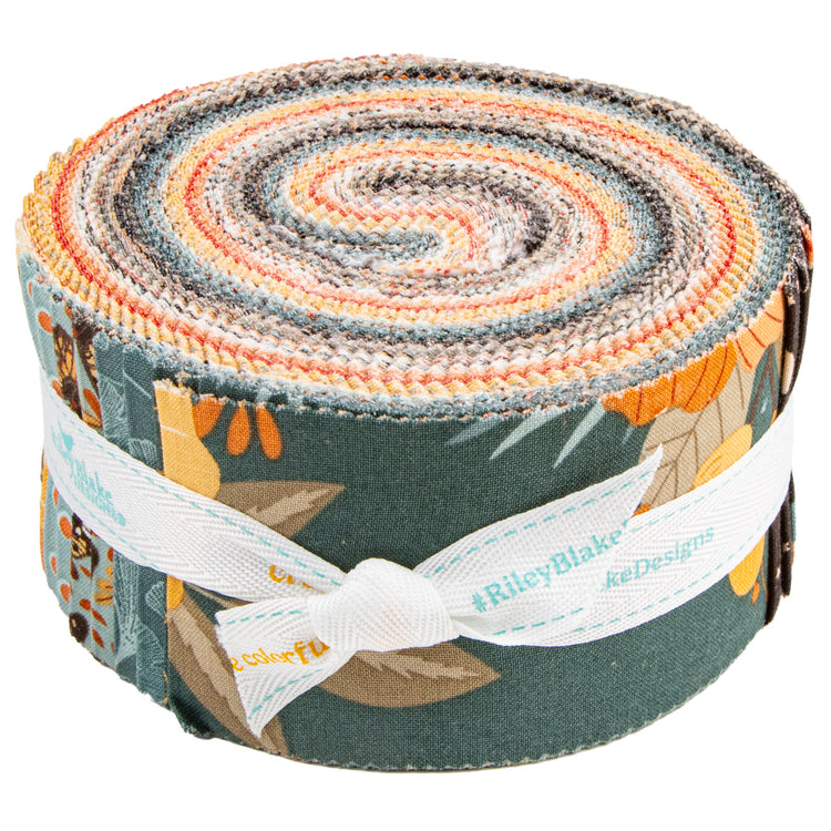 A rolled fabric bundle with a multicolor patterned design featuring orange, yellow, gray, and blue tones, wrapped with a white ribbon printed with the brand name Riley Blake Designs.