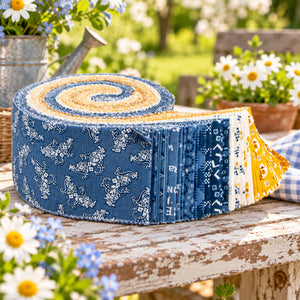 A fabric roll with a blue, white, and yellow patterned design, displayed on a rustic wooden table in a garden setting.