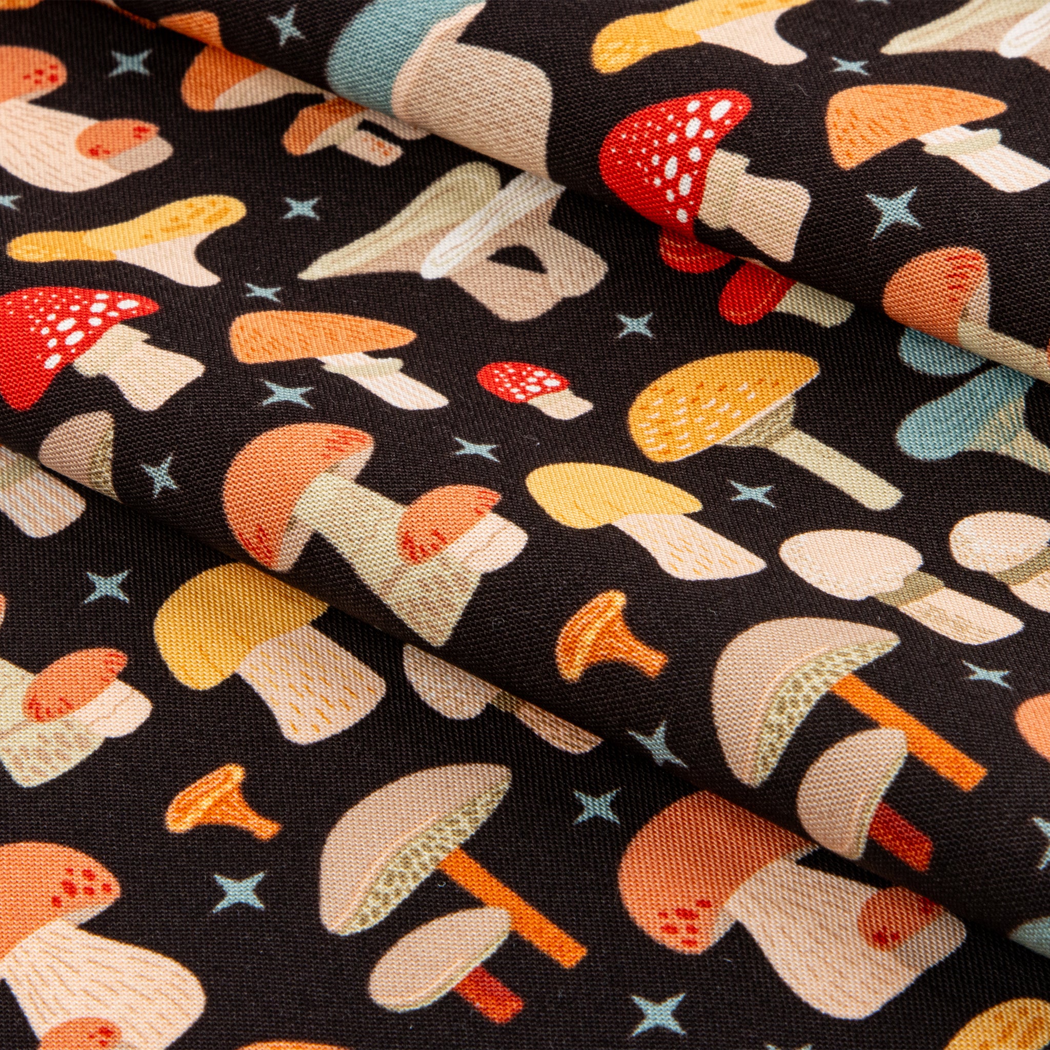 A close-up of a folded black fabric with a colorful mushroom print, showing various mushroom illustrations in orange, yellow, red, and beige, accented with small blue stars.