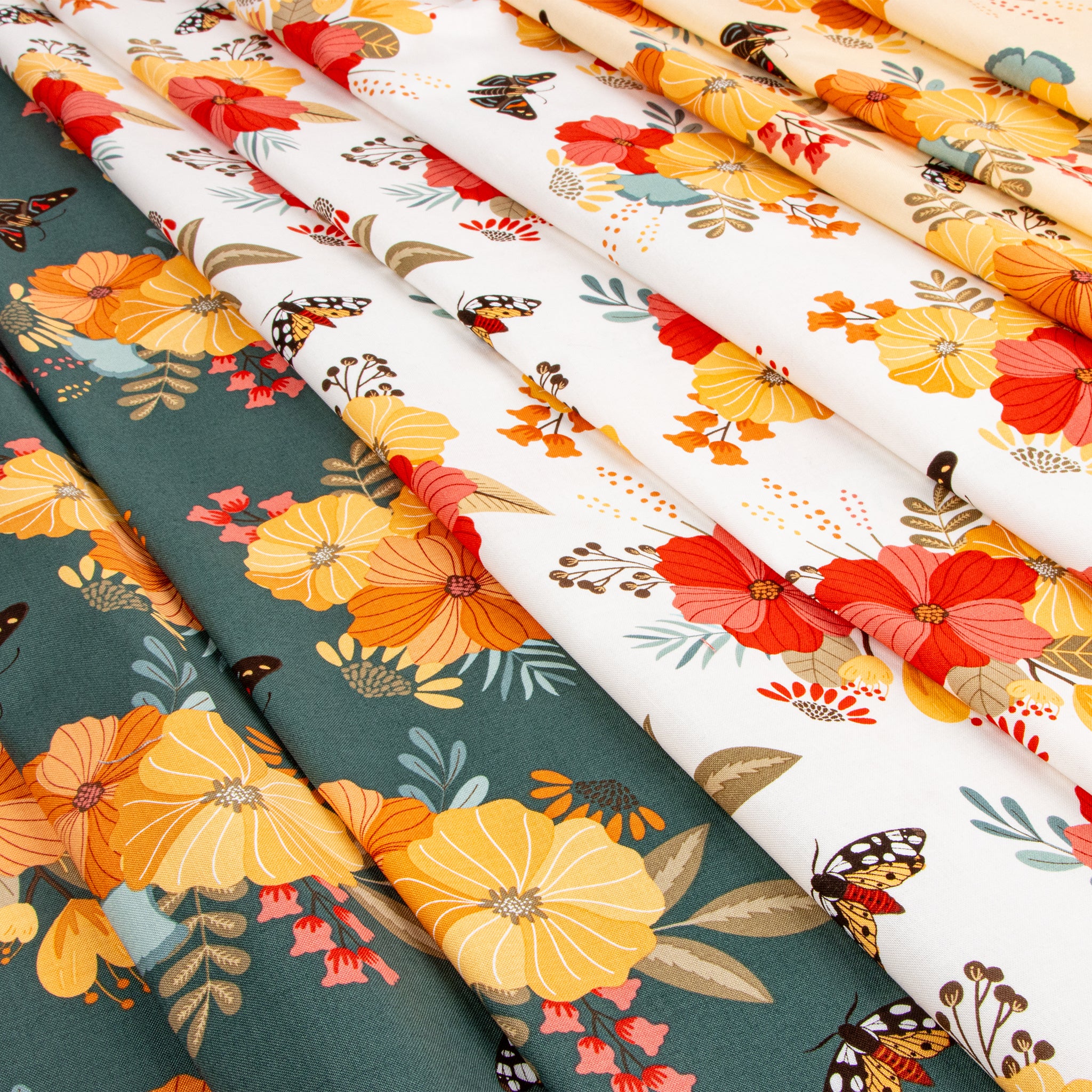 Three folded fabric panels with floral and butterfly prints layered diagonally. The left panel is dark teal with large yellow and orange flowers and green leaves.