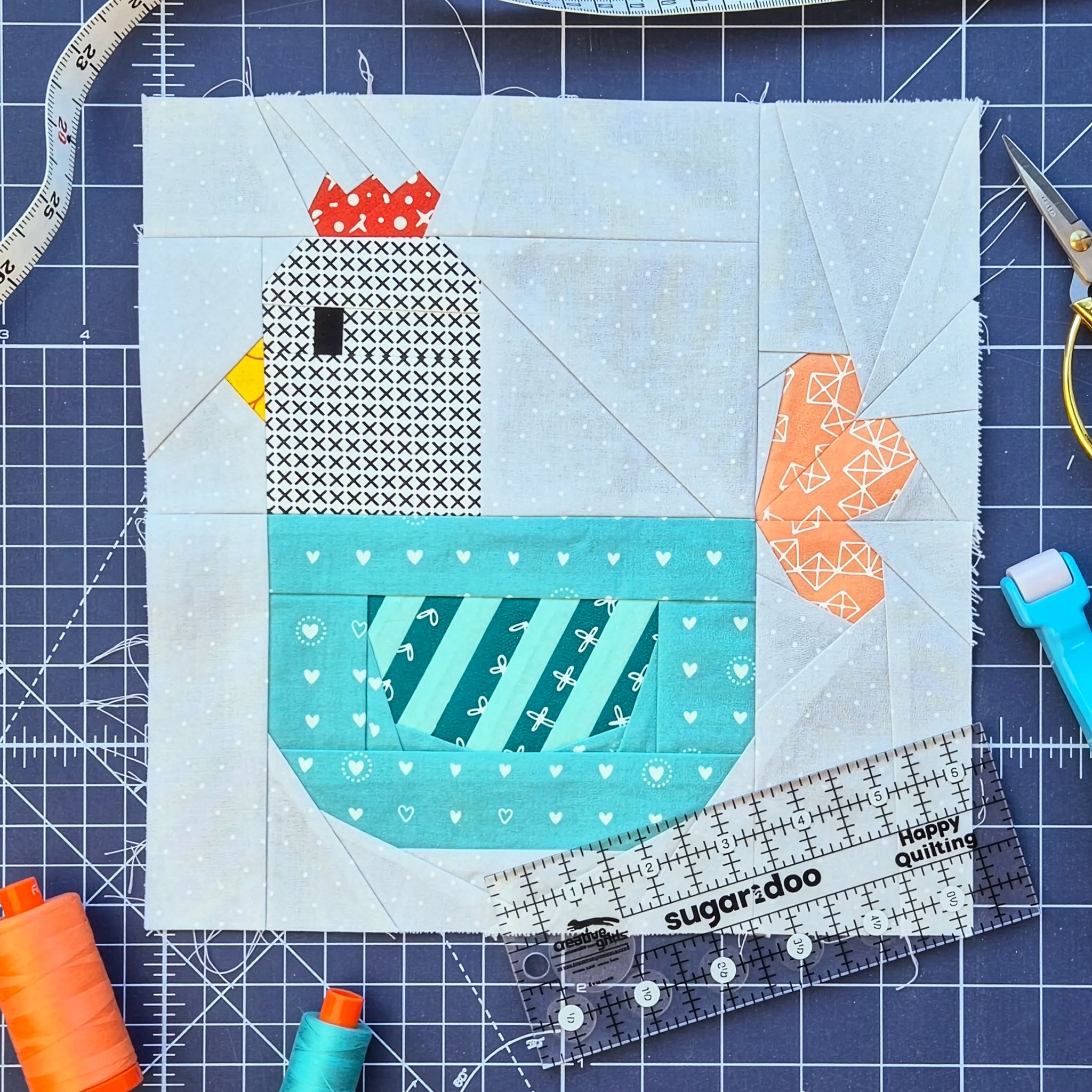 Foundation paper pieced chicken quilt block with ruler, scissors, and sewing tools.
