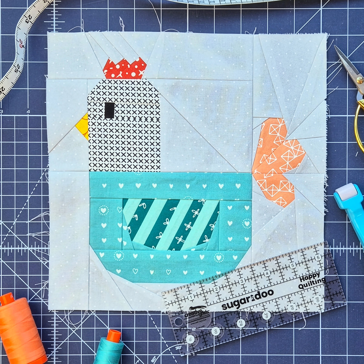 Foundation paper pieced chicken quilt block with ruler, scissors, and sewing tools.