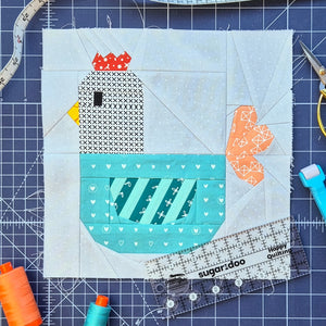 Foundation paper pieced chicken quilt block with ruler, scissors, and sewing tools.