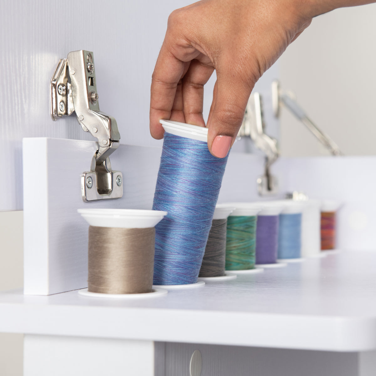 Hand lifting a thread spool from the fold-out thread rack of the Koala Serger Studio cabinet