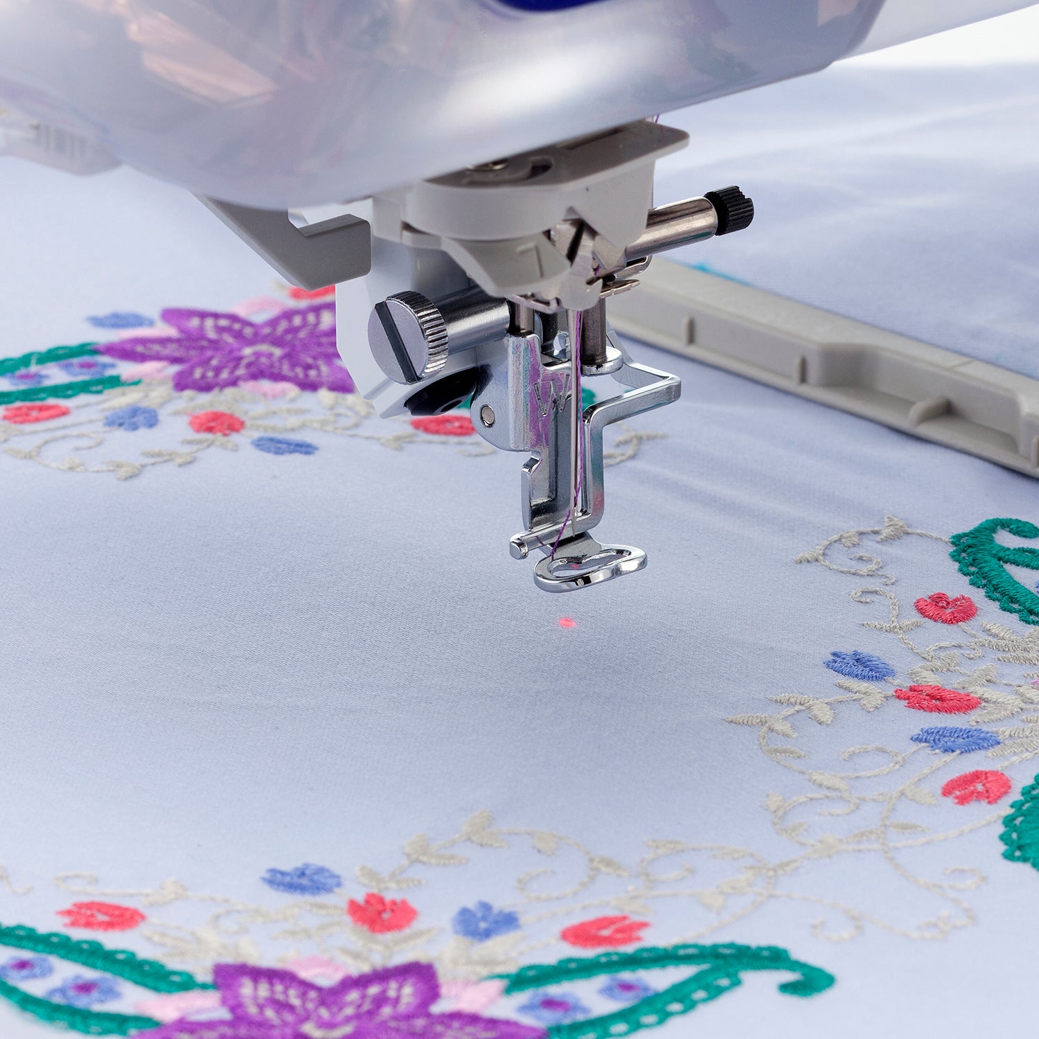 Close up of the needle on a sewing machine with fabric in a hoop in the background. 