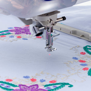 Close up of the needle on a sewing machine with fabric in a hoop in the background. 