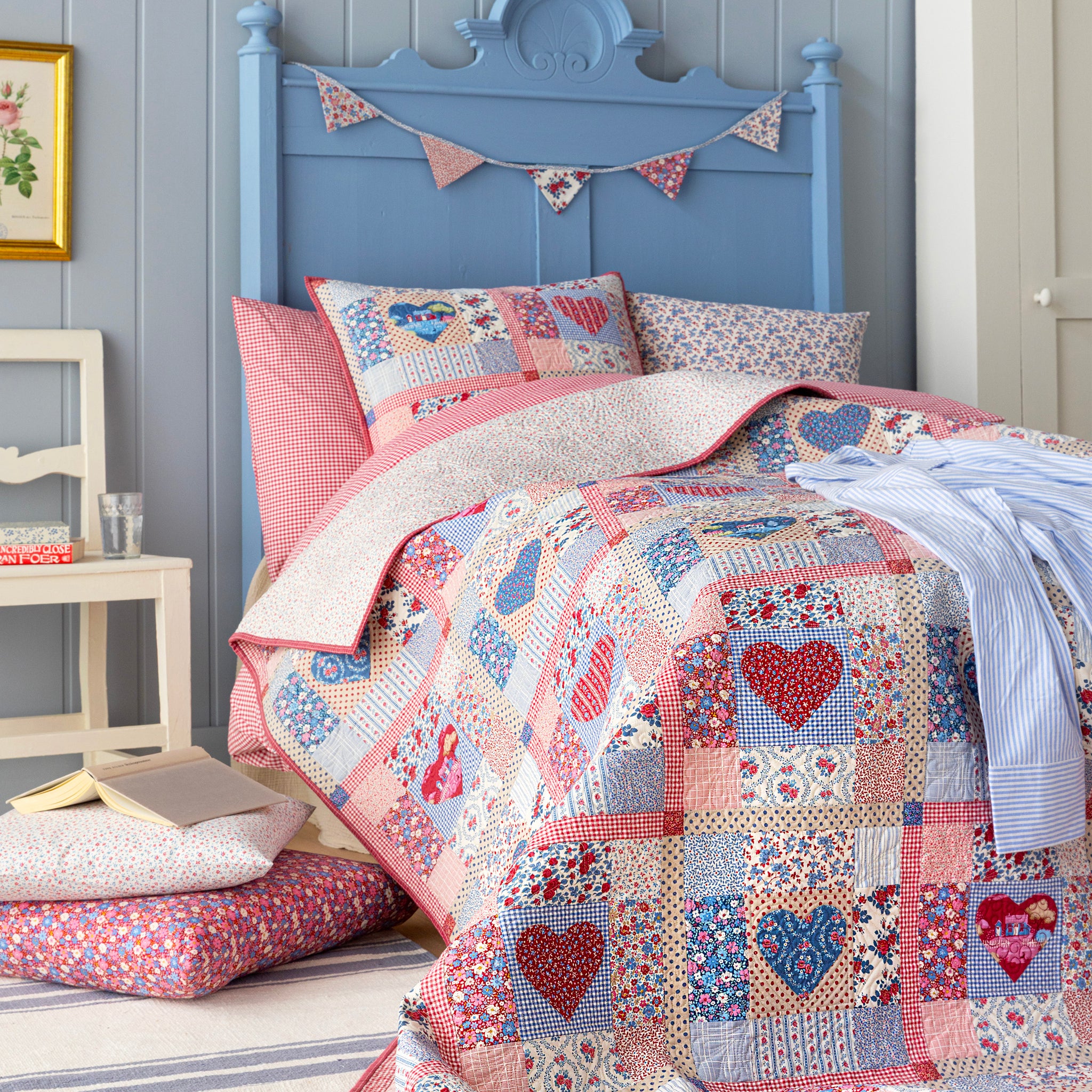 Village Life patchwork quilt with hearts displayed on a blue bed with coordinating pillows.