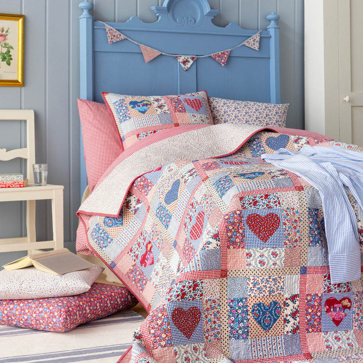 Village Life patchwork quilt with hearts displayed on a blue bed with coordinating pillows.