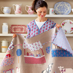Woman holding a Village Life quilt featuring houses, trees and colorful floral prints.