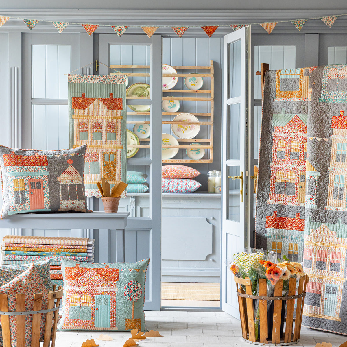 Village Life quilts and pillows displayed in a cozy room with house motifs and floral prints.