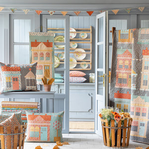 Village Life quilts and pillows displayed in a cozy room with house motifs and floral prints.
