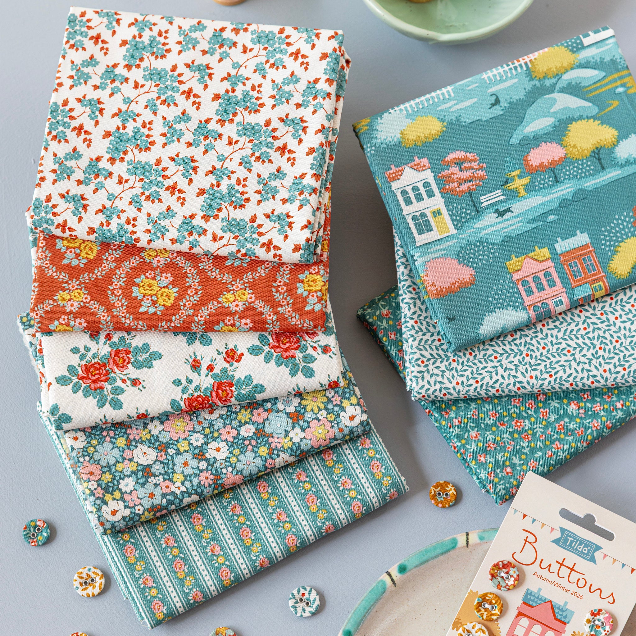 Folded Village Life fabrics in teal, rust and cream floral and village patterns.